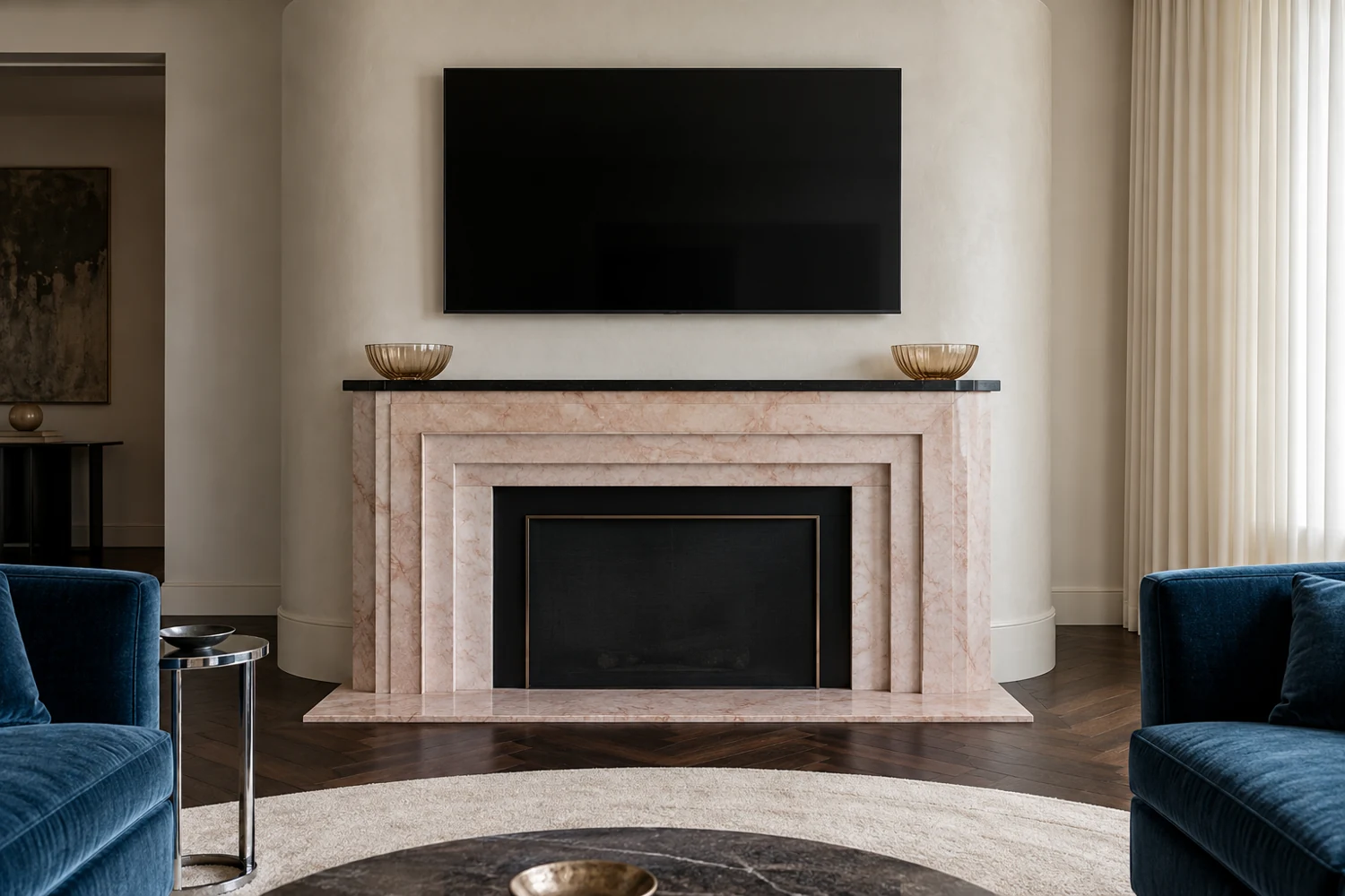 Matching amber glass bowls on a black ledge above a pink marble fireplace, with blue velvet seating and a TV above.